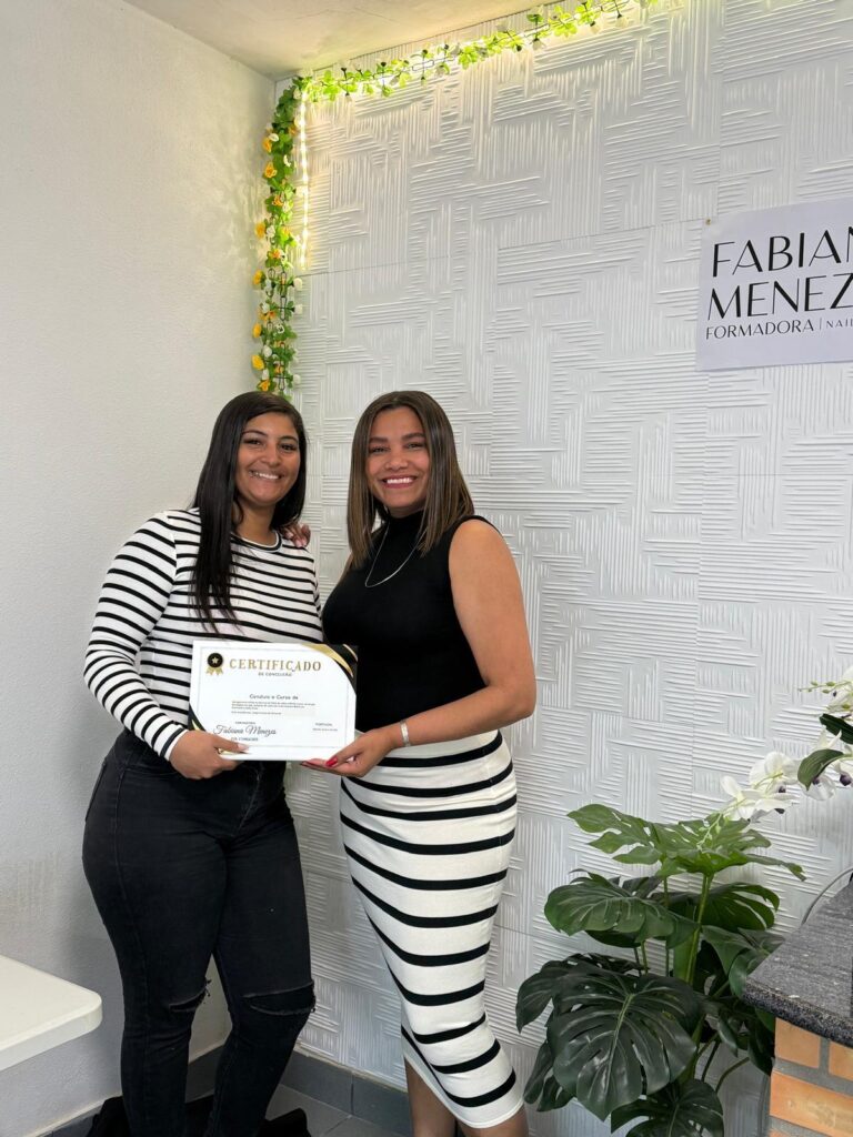 Duas alunas com o certificado, em frente à parede da formação
