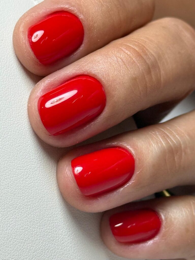 Unhas vermelhas curtas e brilhantes, em grande plano