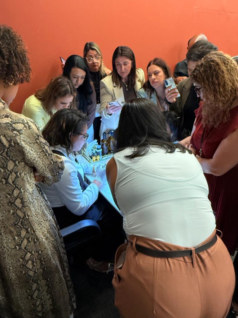Grupo de alunas em volta de uma mesa de trabalho, num workshop