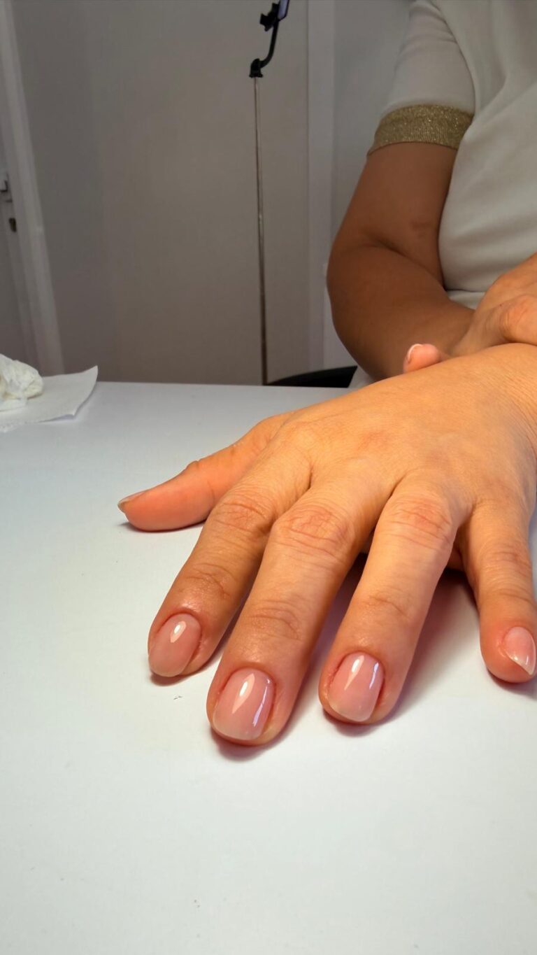Mão pousada numa mesa branca, com unhas nude