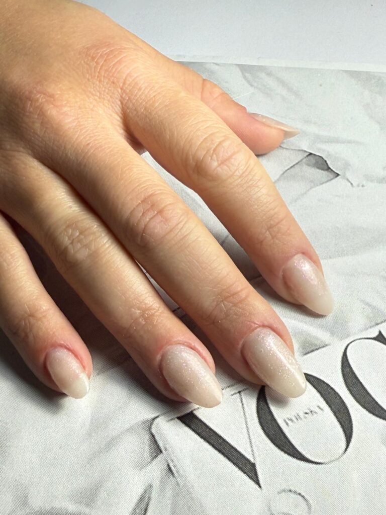 Mão com unhas em amêndoa de tom nude, pousada numa revista